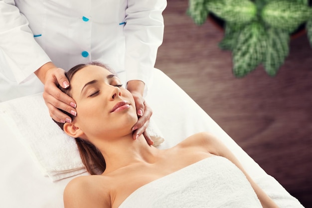 Beautiful young woman receiving face massage in spa salon