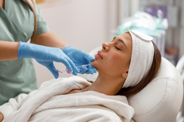 Beautiful young woman receiving hyaluronic acid injection in chin at beauty salon