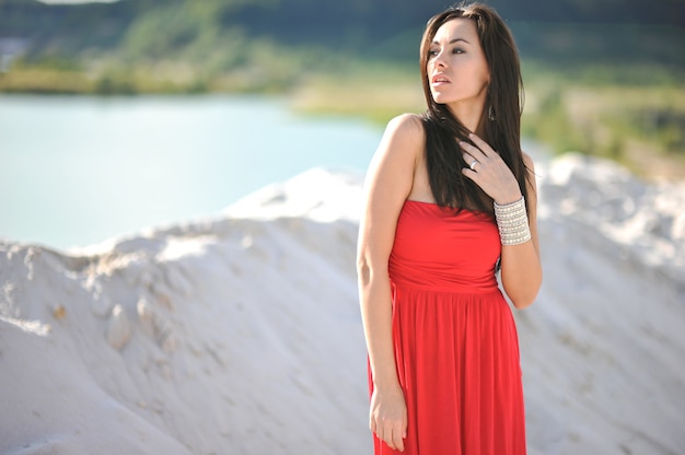 Beautiful young woman in red dress on cloudy background