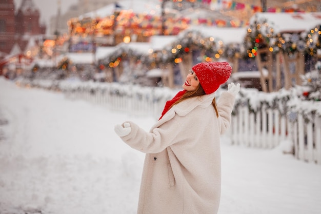 빨간 모자와 따뜻한 옷을 입은 아름다운 젊은 여성이 모스크바 붉은 광장의 크리스마스 박람회에서 즐거운 시간을 보내고 있습니다.