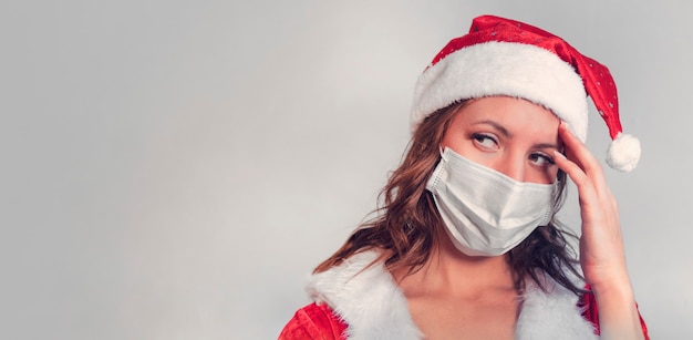 Beautiful young woman in red Santa Claus costume and protective medical mask against virus. Concept of celebrating Christmas in covid 19 pandemic and quarantine. Mrs. Santa sick covid 19. copy space