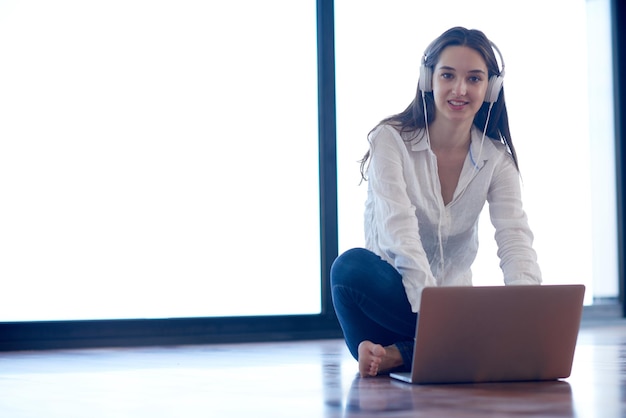 beautiful young woman relax and work on laptop computer modern  home office while listening musin on white headphones