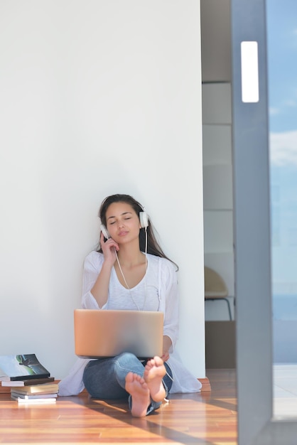 beautiful young woman relax and work on laptop computer while listening music on heaphones and read book at home