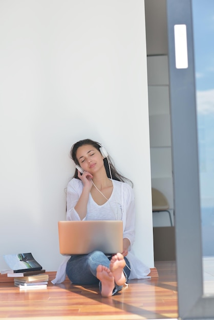 beautiful young woman relax and work on laptop computer while listening music on heaphones and read book at home