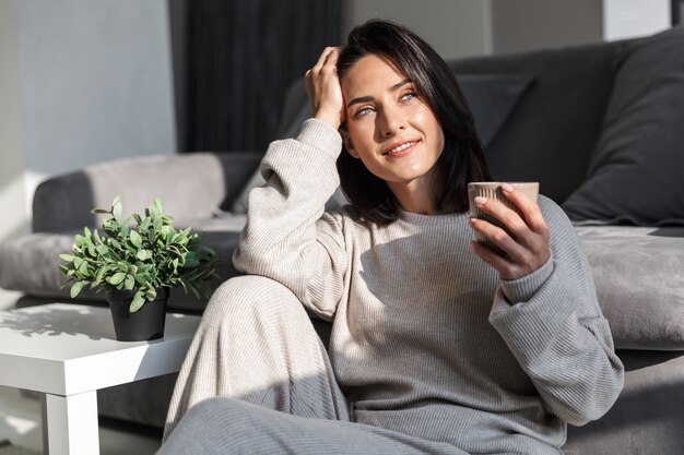 Beautiful young woman relaxing at a couch at home, holding a mug