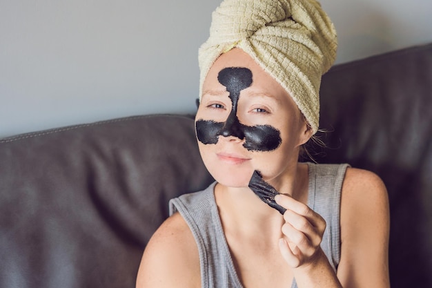 Beautiful young woman relaxing with face mask at home. Happy joyful woman applying black mask on face