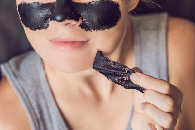 Beautiful young woman relaxing with face mask at home. Happy joyful woman applying black mask on face