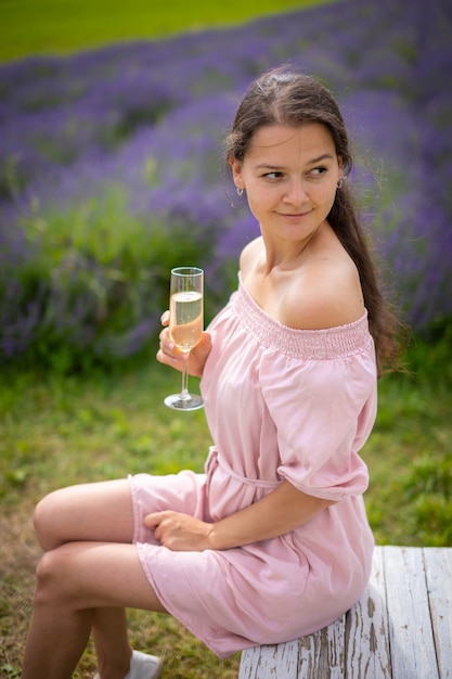 Beautiful young woman resting on a lavender field with glass of champagne in Czech republic