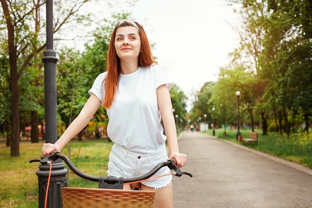 A beautiful young woman rides her bike in the park. Rent transport for the day. Summer, spring. The happy girl smiles. Sport healthy lifestyle, outdoor. sunlight