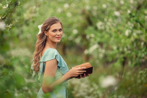 Beautiful young woman in a romantic dress reads a second book in spring in a blooming garden