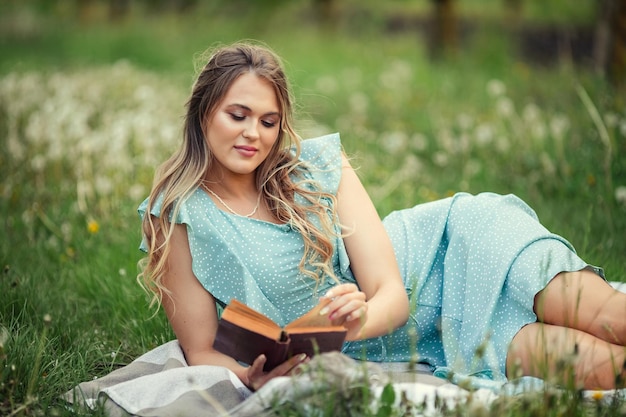 ロマンチックなドレスを着た美しい若い女性は、咲く庭で春に2冊目の本を読みます