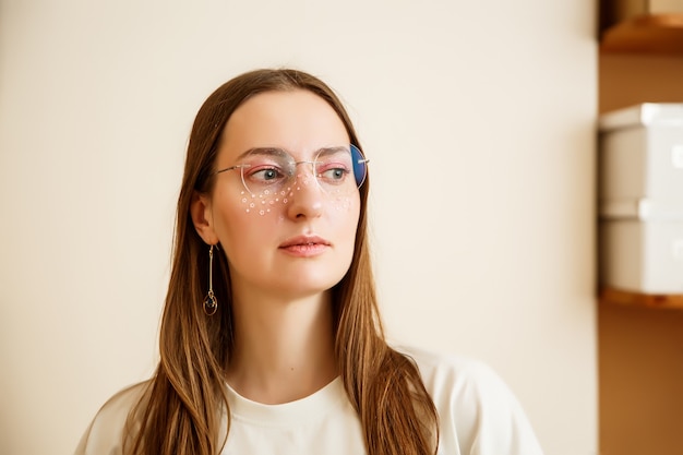 A beautiful young woman in round glasses with pink stars glitter around her eyes