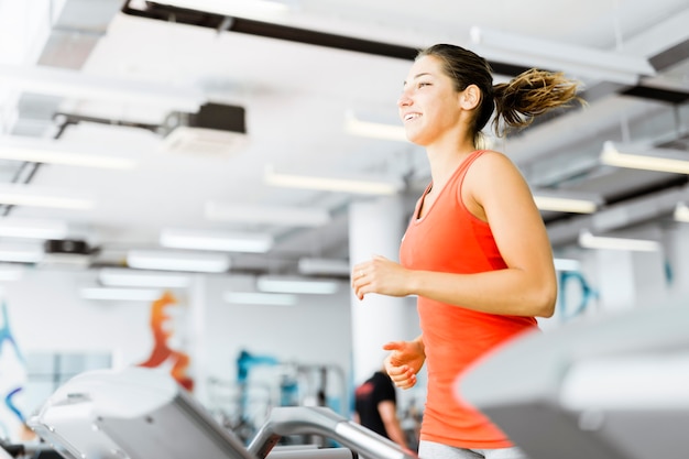 Beautiful young woman running on a treadmill in gym and smiling
