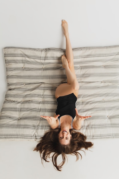 Beautiful young woman's portrait on grey mattress in studio. Having fun, happy, full length