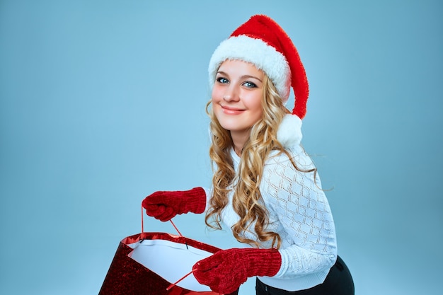 Beautiful young woman in Santa Claus clothes with a gift on blue