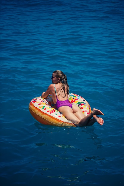 Beautiful young woman in the sea swims on an inflatable ring
and has fun on vacation girl in a bright swimsuit at the sea under
the sunlight