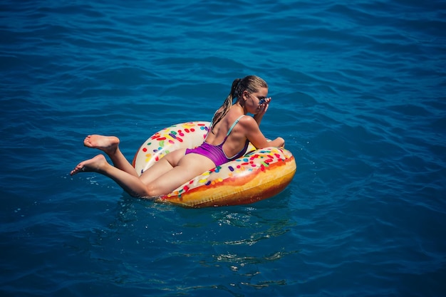 Bella giovane donna in mare nuota su un anello gonfiabile e si diverte in vacanza ragazza in un costume da bagno luminoso al mare sotto la luce del sole