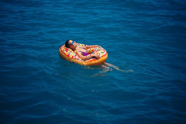 Beautiful young woman in the sea swims on an inflatable ring
and has fun on vacation girl in a bright swimsuit at the sea under
the sunlight