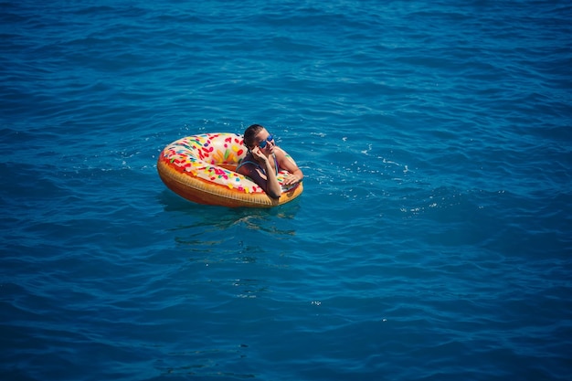 Bella giovane donna in mare nuota su un anello gonfiabile e si diverte in vacanza ragazza in un costume da bagno luminoso al mare sotto la luce del sole Foto Premium