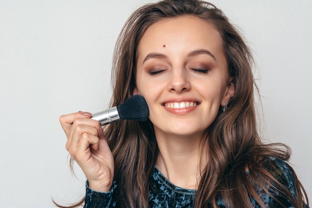 Beautiful young woman in shiny green dress applying powder with a brush to the face.