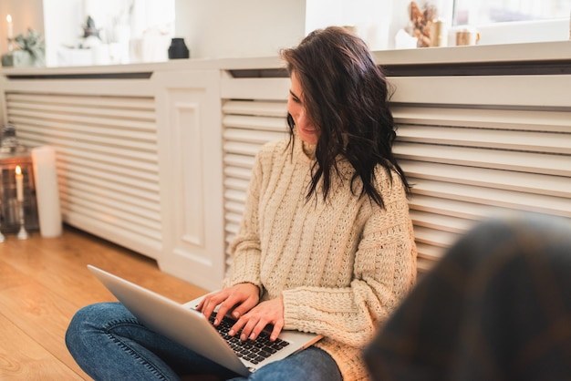 Beautiful young woman shopping online on laptop in cozy Christmas interior Female sitting on the floor bying gifts for the family on winter sales via computer using wireless Internet Copy space