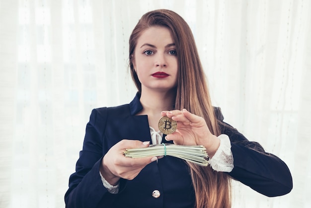 Beautiful young woman showing bitcoin and dollar banknotes