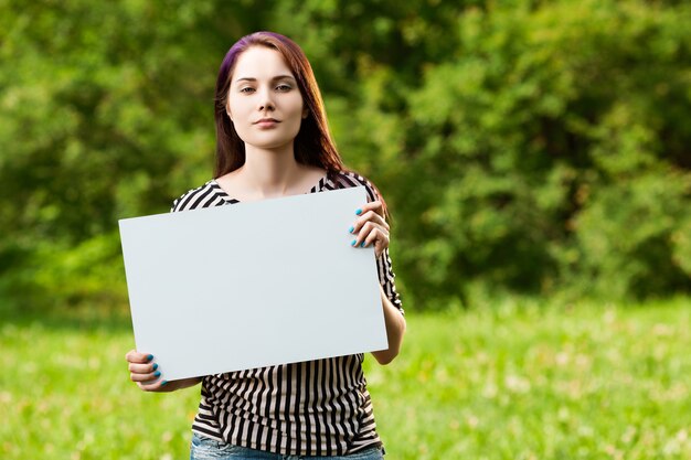 Beautiful young woman showing a blank white board, outdoors