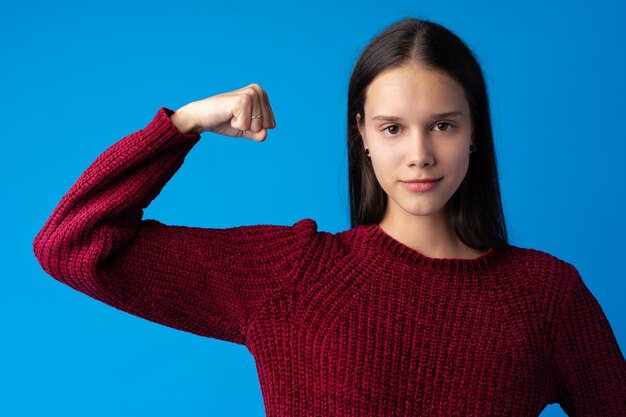 beautiful young woman showing her muscularity and looking at camera on blue background
