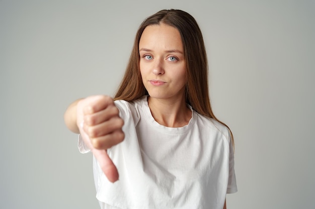 Beautiful young woman showing thumbs down sign to dislike on gray background