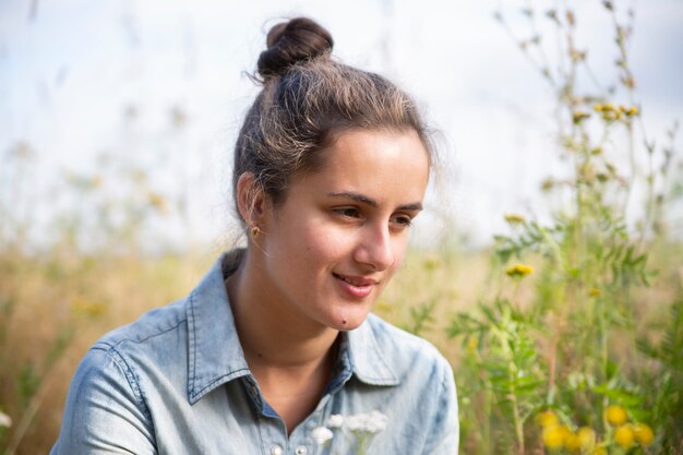 beautiful young woman sits in a meadow in flowers on a sunny summer day and smiles.