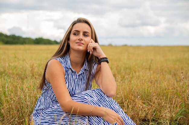 Beautiful young woman sits in a meadow in flowers on a sunny summer day and smiles