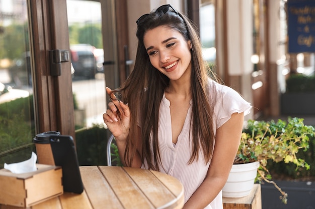 屋外のカフェテーブルに座っている美しい若い女性