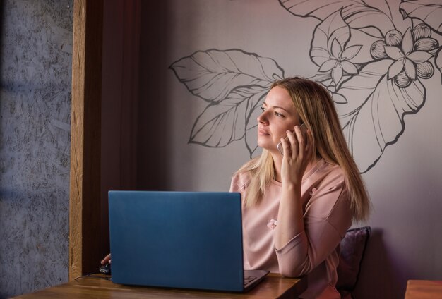 Beautiful young woman sitting in a cafe with a laptop and talking on the phone