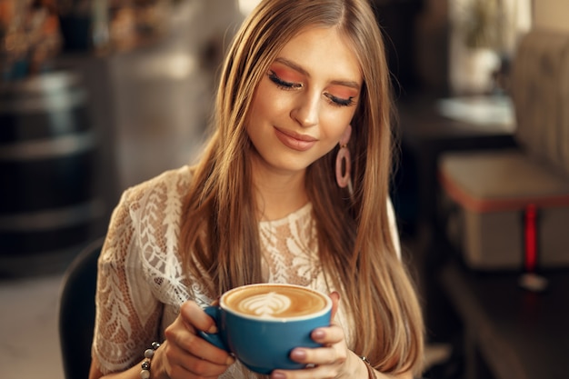 彼女の飲み物を楽しんでいるコーヒーショップに座っている美しい若い女性