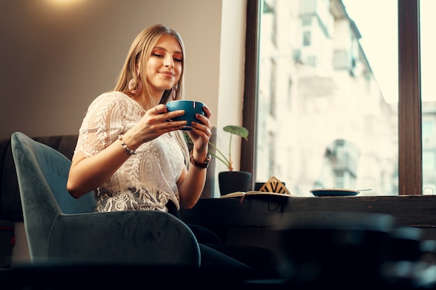 Bella giovane donna che si siede nella caffetteria che gode del suo drink