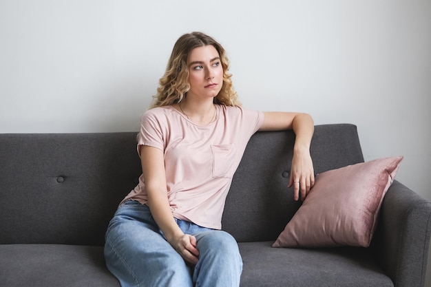 Beautiful young woman sitting on gray sofa in the room Resting girl in pink shirt Relaxing woman