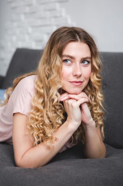 Beautiful young woman sitting on gray sofa in the room Resting girl in pink shirt Relaxing woman