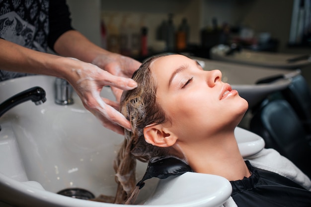 Foto bella giovane donna che si siede vicino al lavandino mentre parrucchiere che lava i suoi capelli nel salone di bellezza