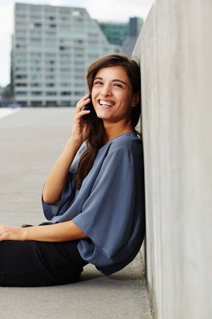 Beautiful young woman sitting outdoors and talking on cell phone