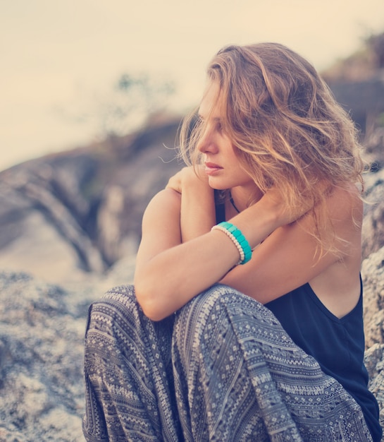 Beautiful young woman sitting on the rocks at sunset 