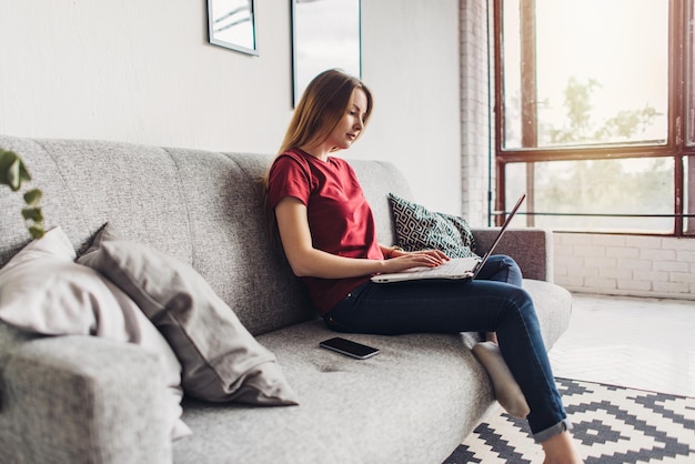 Beautiful young woman sitting on sofa and using laptop at home