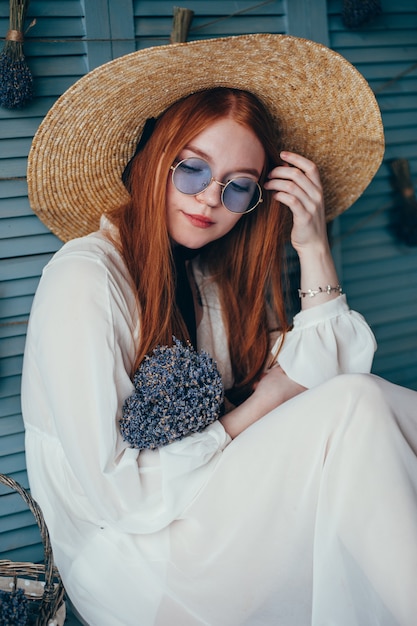 Bella giovane donna che si siede con la lavanda contro la parete blu.