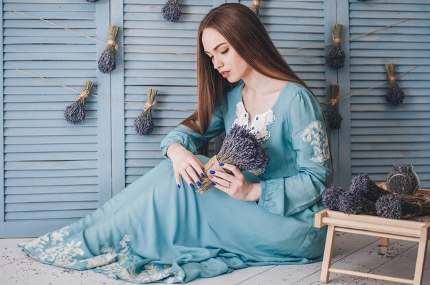 Beautiful young woman sitting with lavender against the blue wall. 