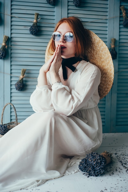 Bella giovane donna che si siede con la lavanda contro la parete blu.