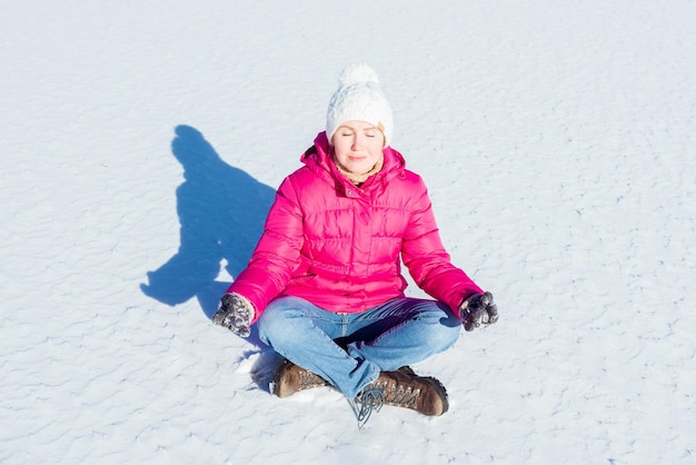 Bella giovane donna seduta in una posizione yoga su un lago ghiacciato nel paesaggio delle montagne di neve, meditando e contemplando il paesaggio durante una giornata invernale in vacanza, all'aperto