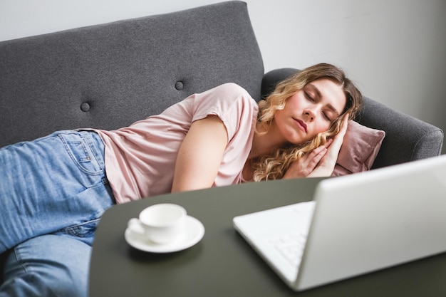 Beautiful young woman sleeping on gray sofa Girl in pink shirt resting at home after work