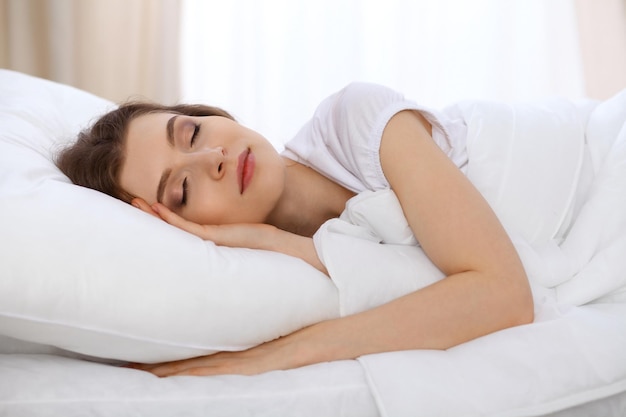 Beautiful young woman sleeping lying in bed and relaxing in the morning. A sunny day starts is the time to go for a work or sleep on the weekends.