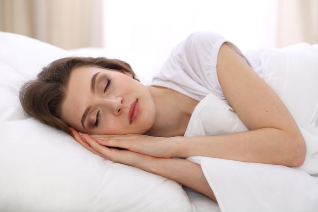 ベッドに横になって快適にリラックスしながら寝ている美しい若い女性。仕事や休日に目覚めるのは簡単です。アクティブな生活のための快適で休息の回復の概念。