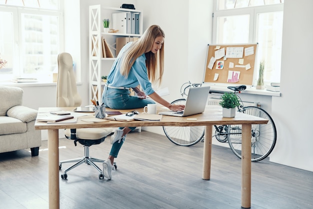 Красивая молодая женщина в элегантной повседневной одежде, используя ноутбук во время работы в офисе
