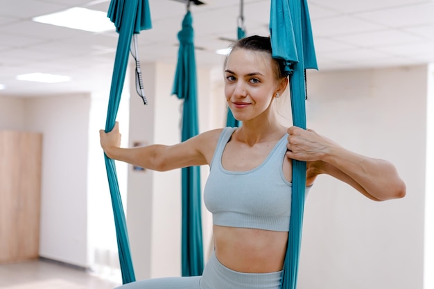 Bella giovane donna sorridente che guarda l'obbiettivo e usa l'amaca per lo yoga